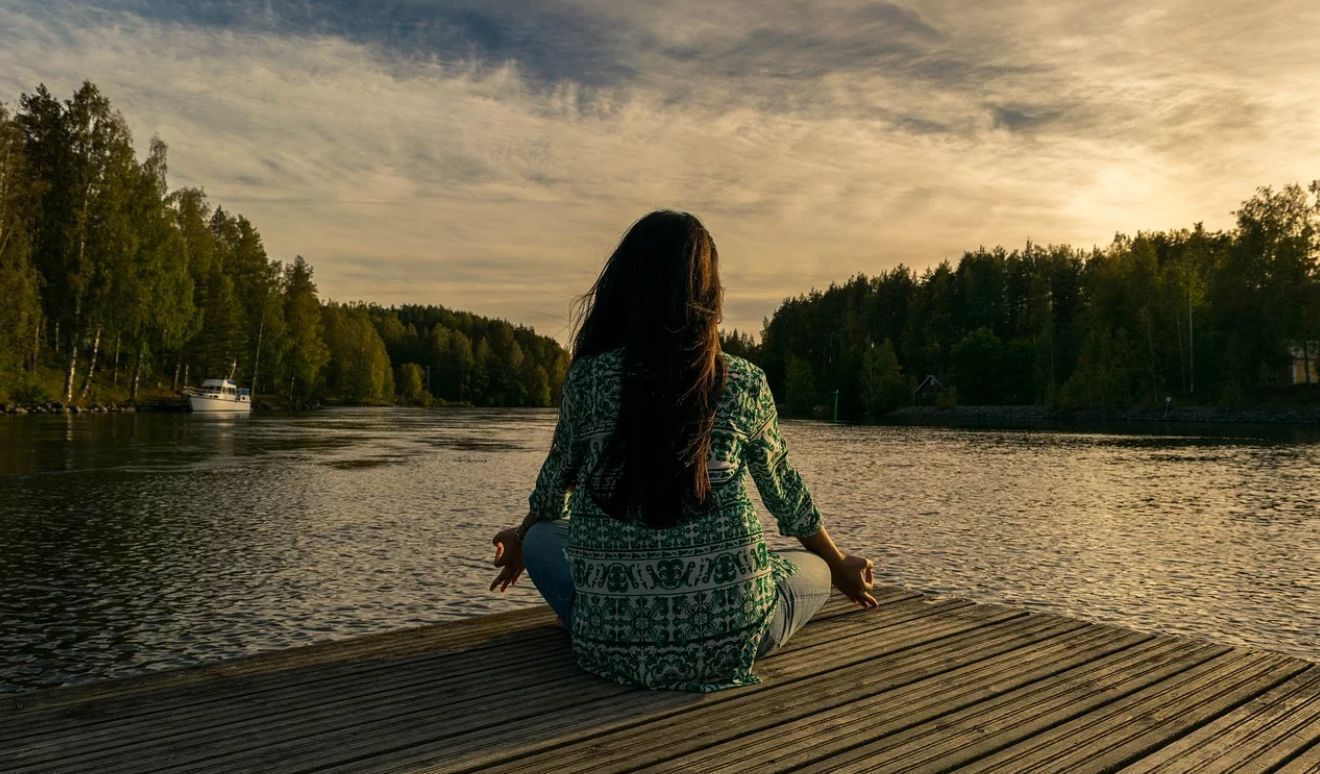 devojka sedi pored vode i meditira